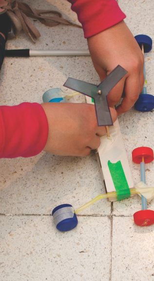 Manos de chicos armando un vehículo de juguete con tapitas de colores y sorbetes