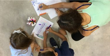 Vista cenital de una madre y sus hijas dibujando juntas sobre el piso